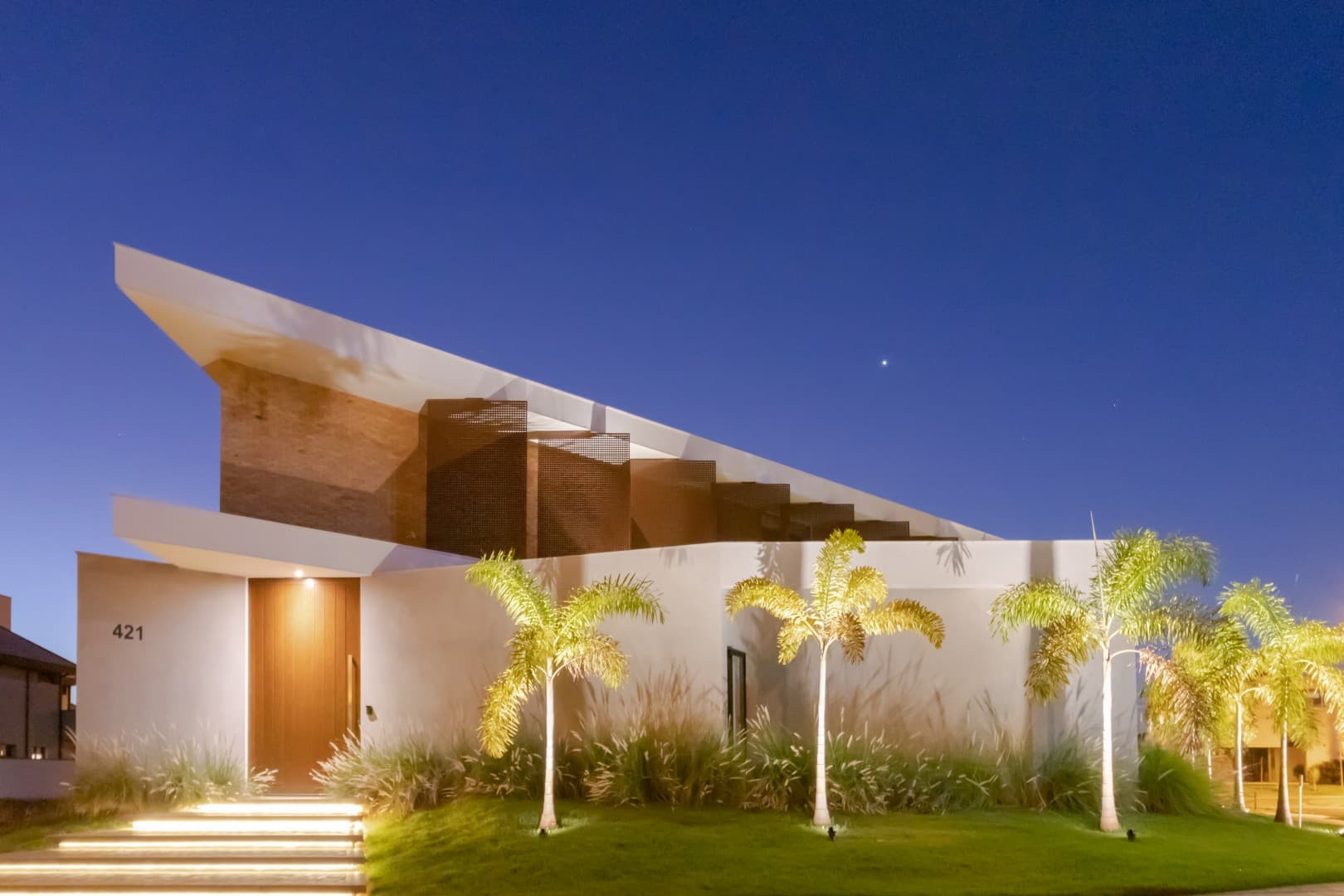 Casa CaCle – fachada noturna com cobogós iluminados e paisagismo