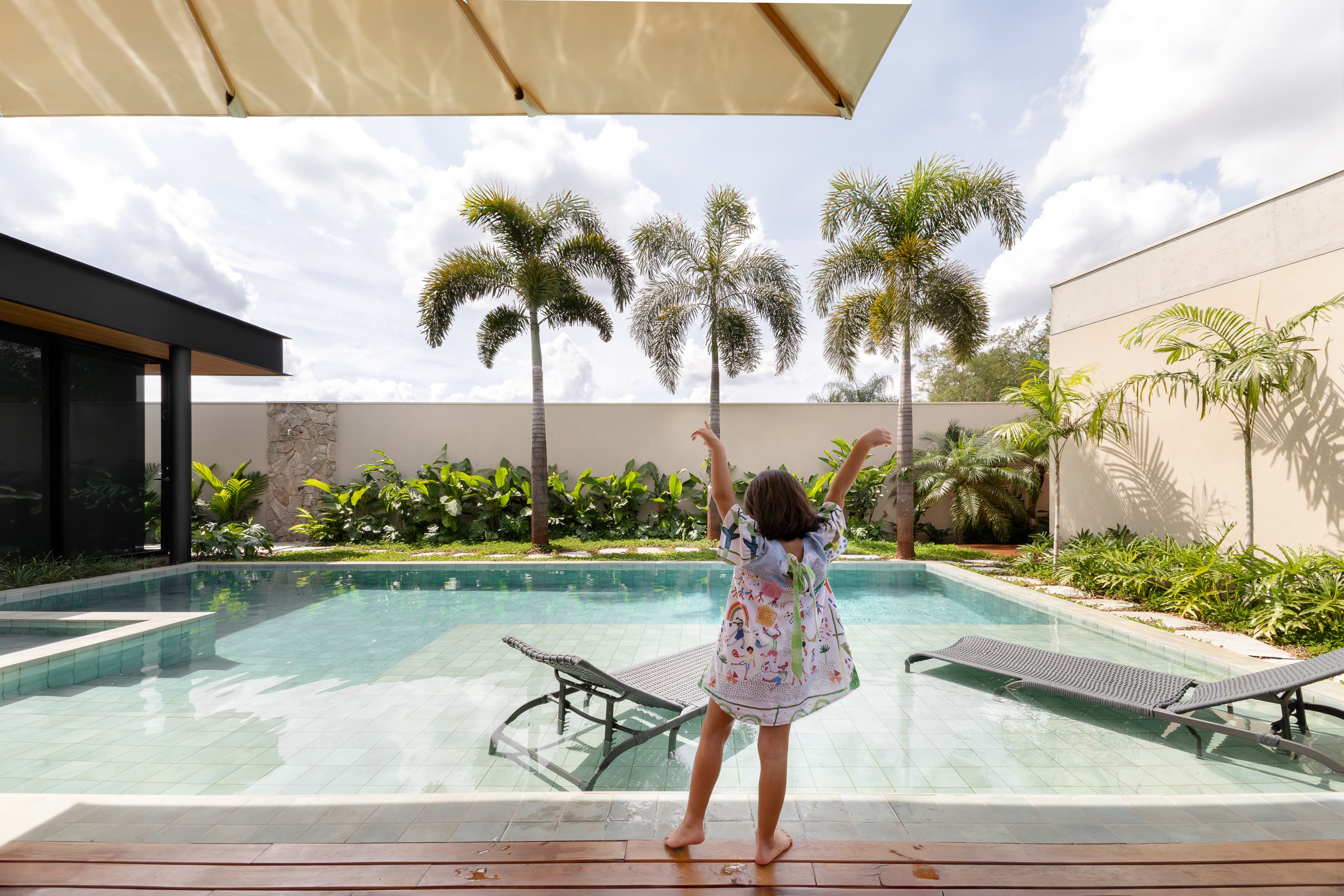 Casa LuSi – área de piscina com palmeiras, jardim exuberante e moradora