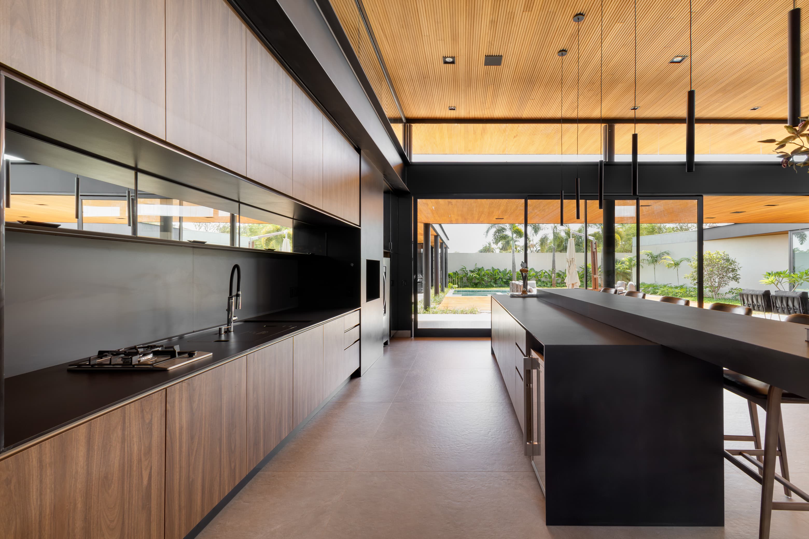 Casa LuSi – cozinha escura com bancada preta e abertura para jardim externo
