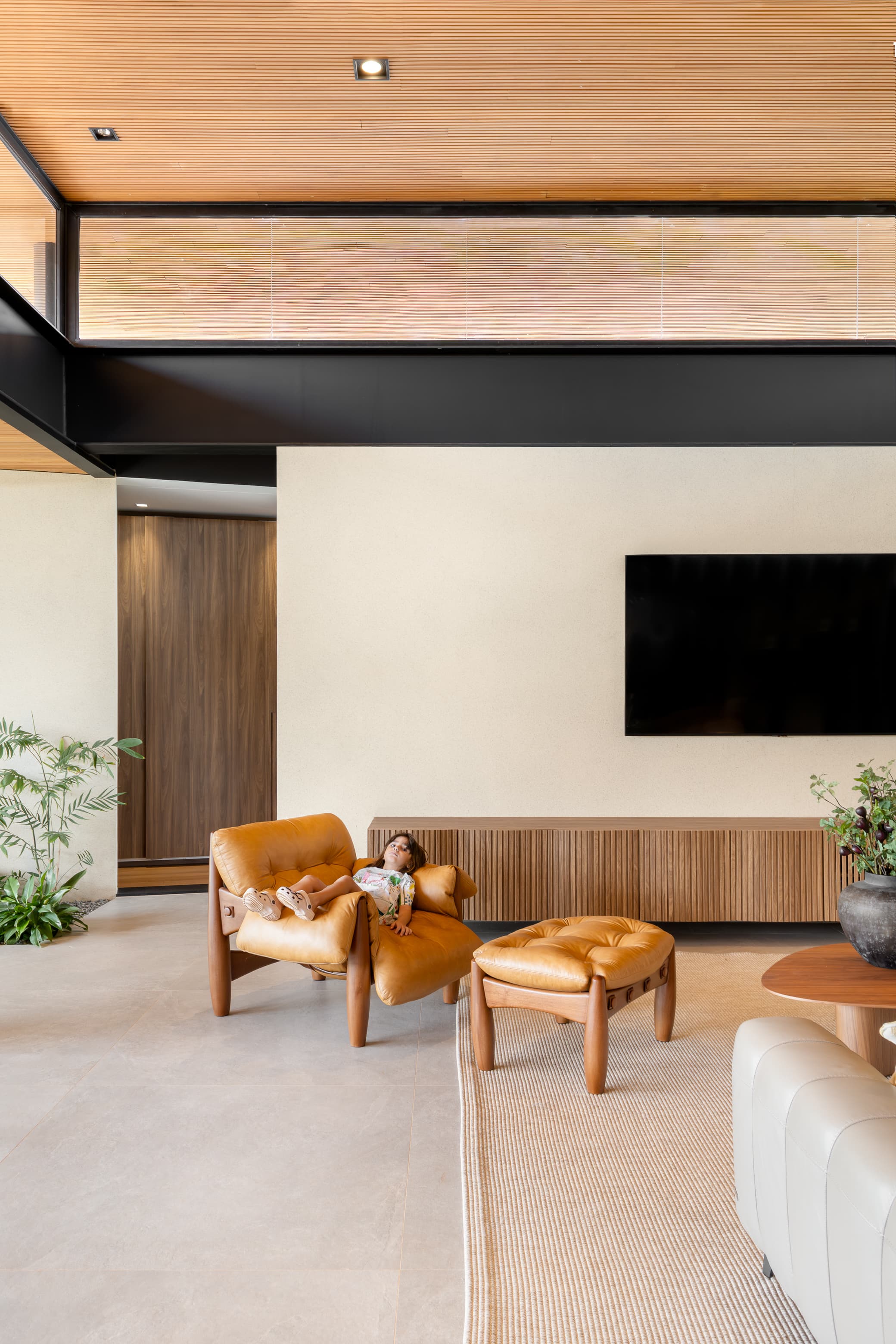 Casa LuSi – painel de madeira com TV embutida e jardim com plantas tropicais