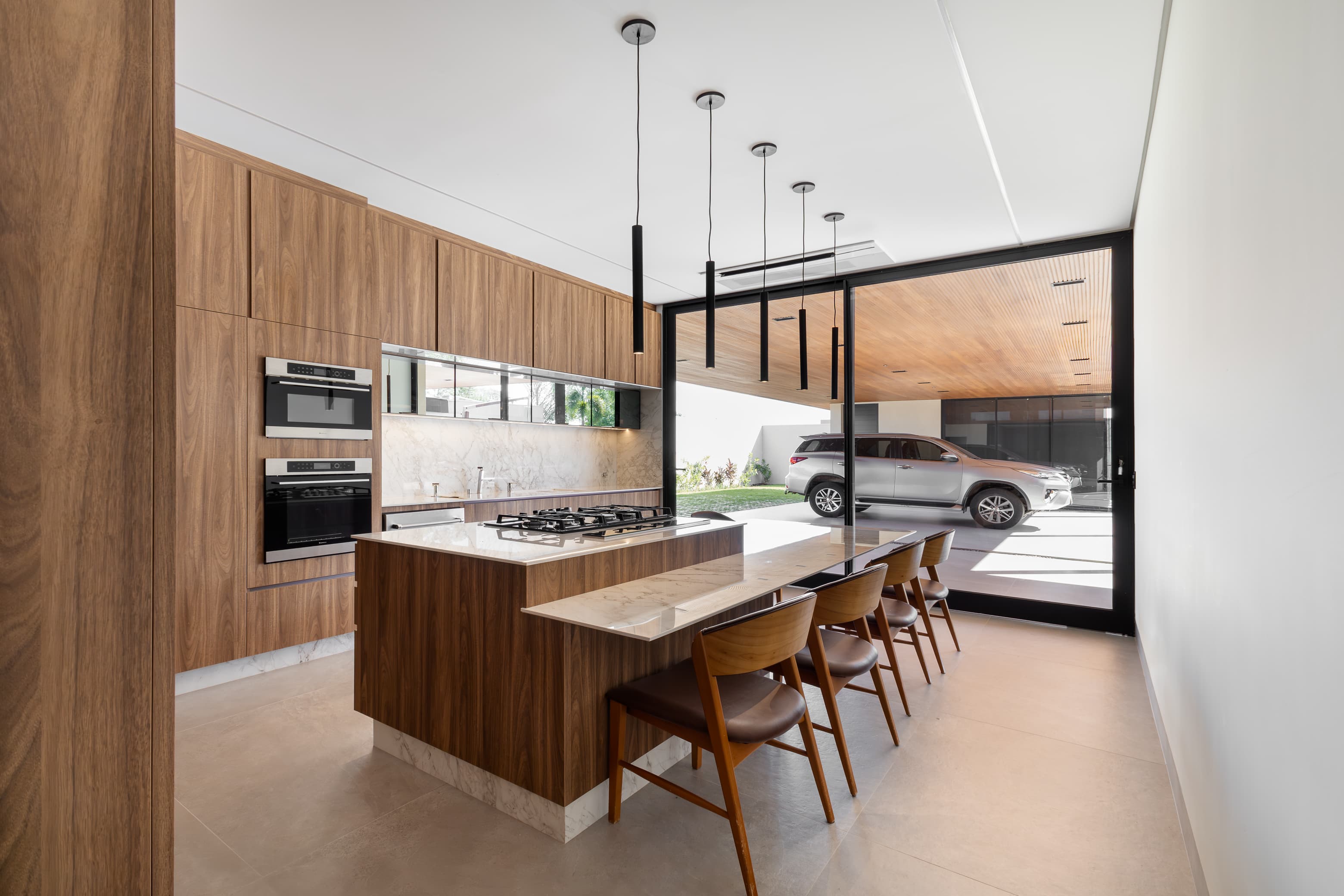 Casa LuSi – cozinha com marcenaria em madeira, ilha e vista para garagem