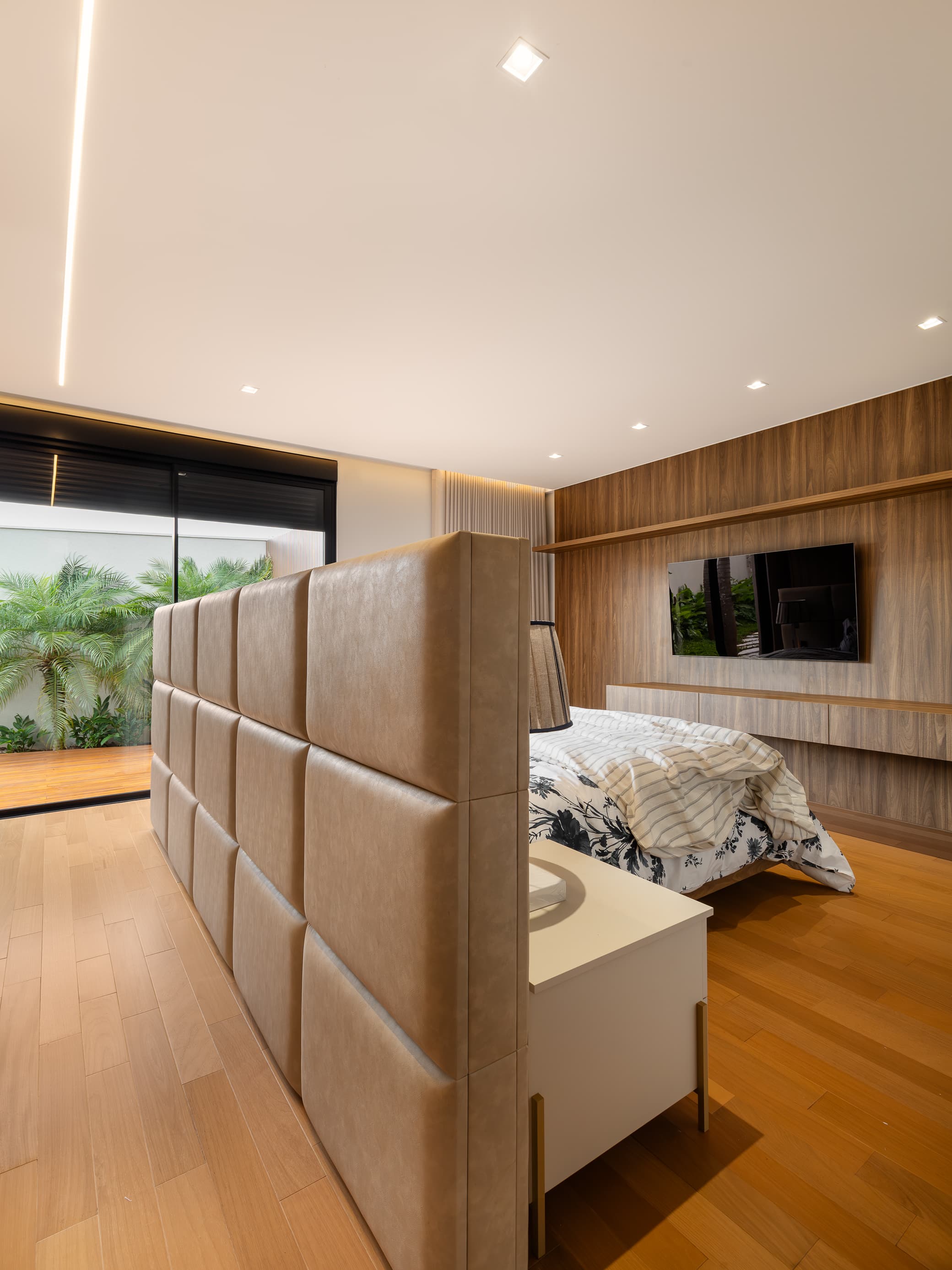Casa LuSi – suíte com cabeceira estofada bege, jardim e painel de TV em madeira